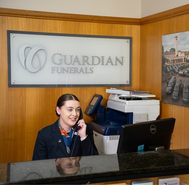 funeral director talking on the landline infront of a guardian funerals sign
